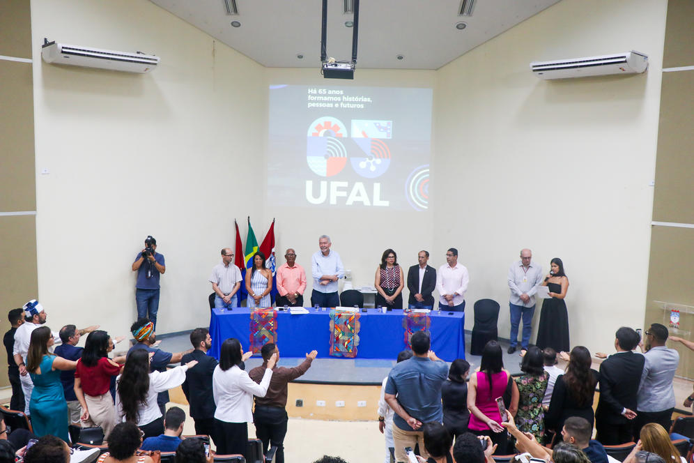 Na foto, os novos servidores da Ufal est&atilde;o em p&eacute;, com a m&atilde;o direita erguida, durante leitura do termo de compromisso. 